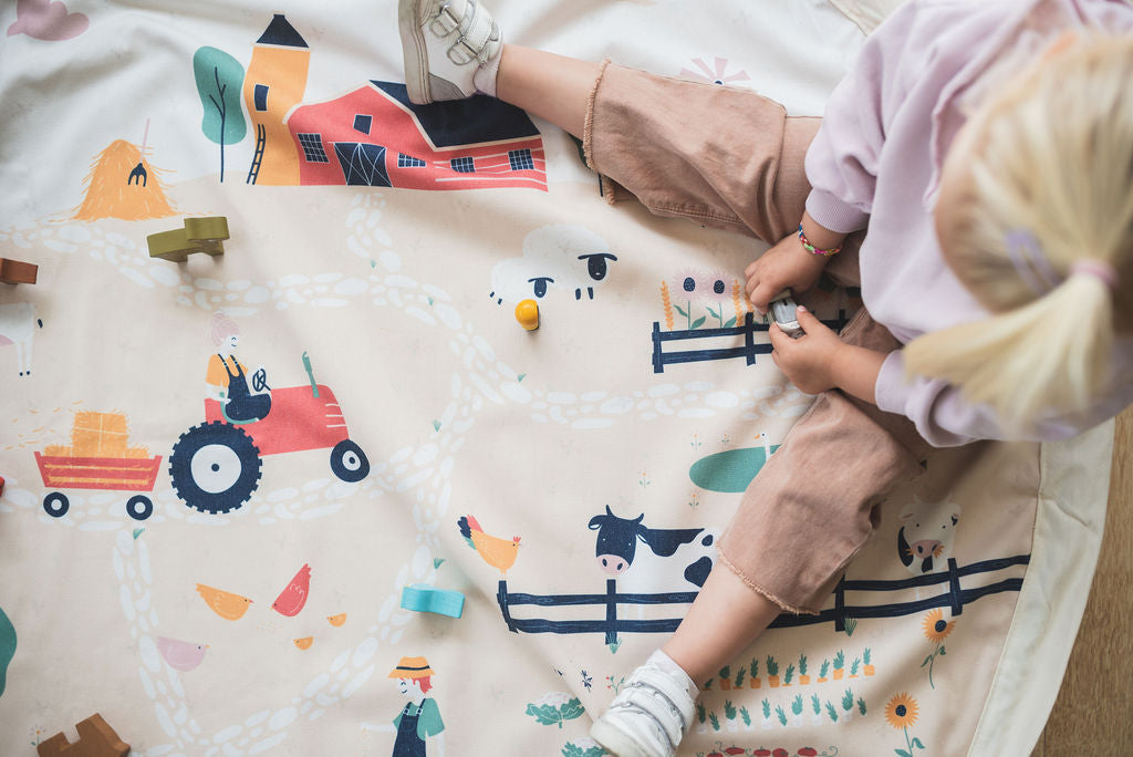 farm toy storage bag and play mat, child sitting and playing on mat with wooden toys