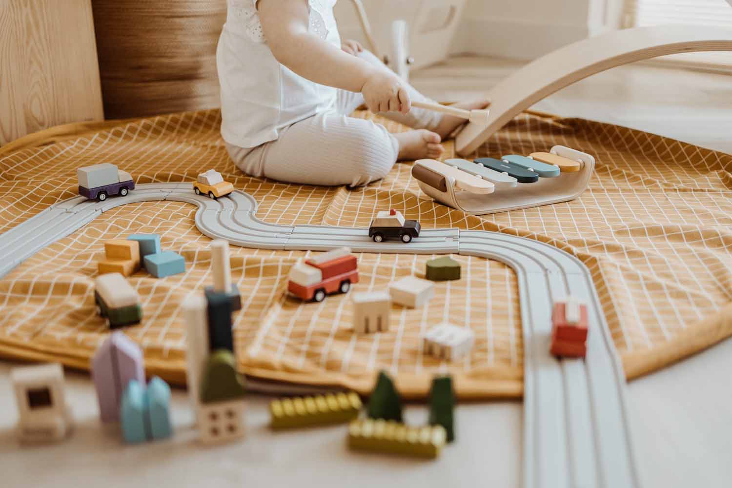 open organic grid mustard storage bag, child playing with wooden toys, wooden cars on road