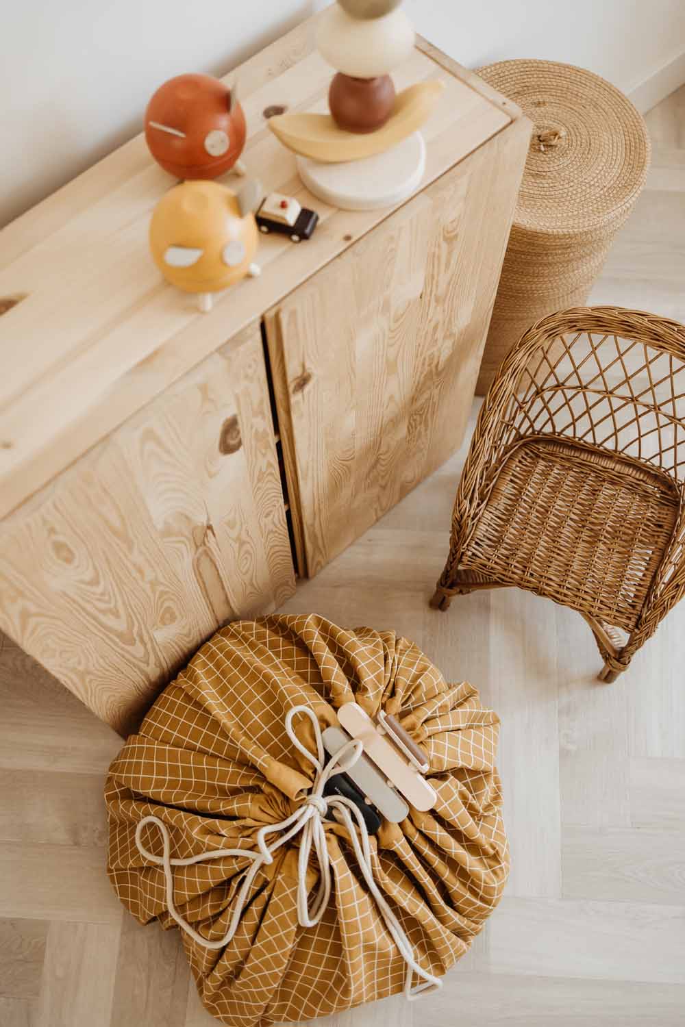 closed organic grid mustard storage bag, on floor, next to wooden closet and wicker chair