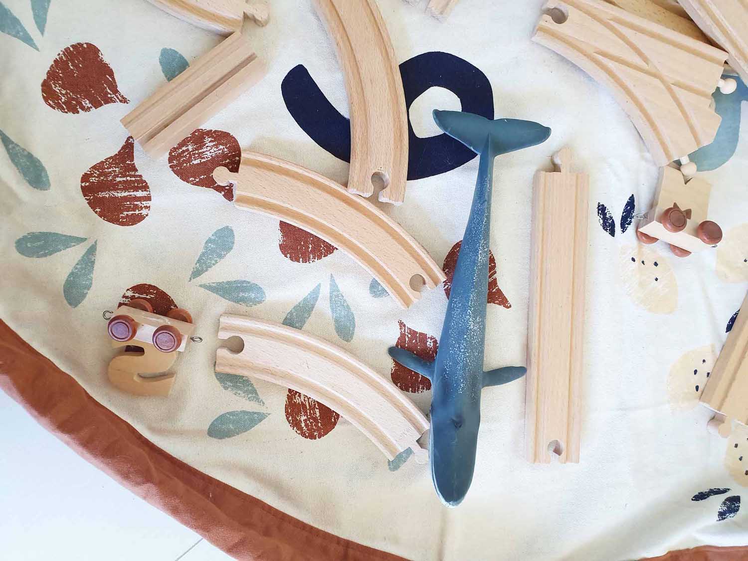 veggie numbers storage bag, open on floor, toy of a whale and wooden train rails on mat