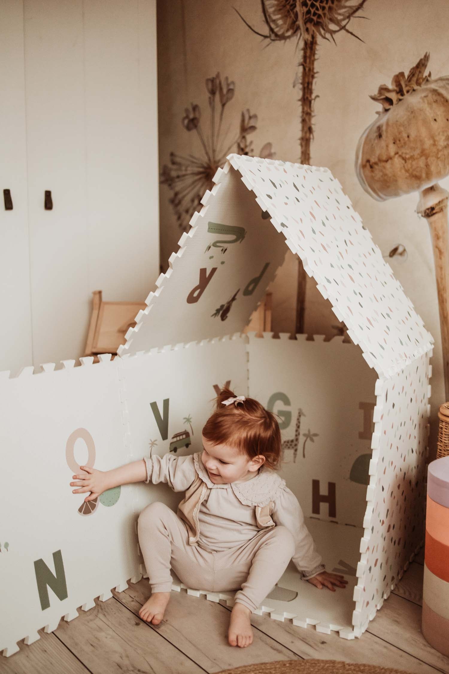 child playing with alphabet/terrazzo puzzlemat, mat made as a house, child opening the door