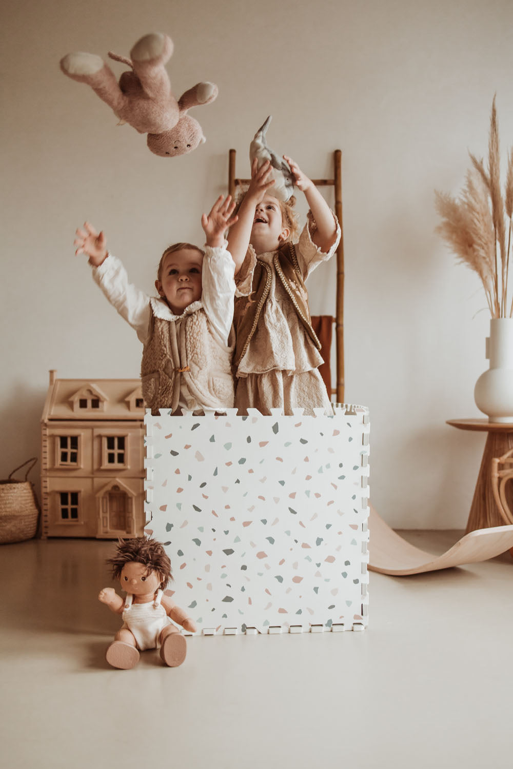 children standing in box made of terrazzo puzzlemat, throwing cuddles in the air